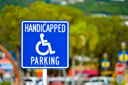 A bright blue handicapped parking sign showing wear with foliage blurred in the background の写真素材