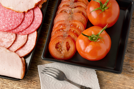 Various sausages and tomatoes placed on black ceramic platesの写真素材