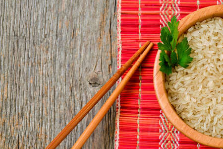 Bowl with brown uncooked rice and leaf of parsleyの写真素材