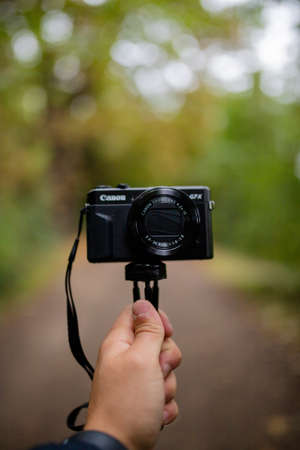 Portrait View of a Hand Holding a Camera with a Blurry Forest as Backgroundのeditorial素材