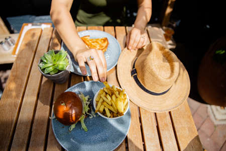 Woman Hands Reaching out for Hamburger and Fries on a Wooden Tableの写真素材