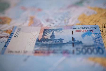 Fifty thousand rupiah bill on top of Indonesia on a colorful and blurry map