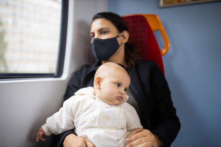 Woman sitting next to a window in a bus and holding her baby in her armsの写真素材