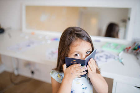 Little girl in front of a desk hides her face behind an American passport