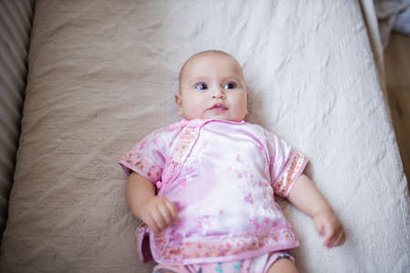 Curious and adorable baby girl in Asian pink attire lying down on a bed