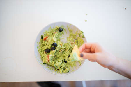 Female hand dipping nachos in guacamole sauce with olivesの写真素材