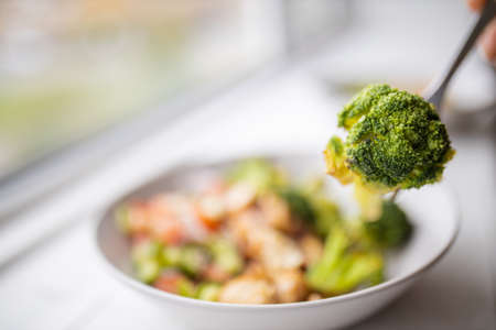 Fork picking broccoli from a broccoli and chicken salad next to a windowの写真素材