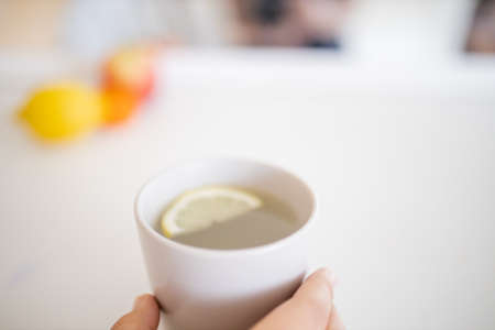 Hand holding a cup of lemon tea with a lemon slice insideの写真素材