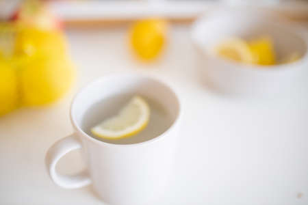 Cup of lemon tea on a white table surrounded by lemonsの写真素材