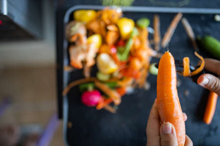 Female hands peeling a carrot on top of organic trashの写真素材