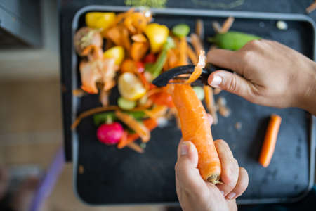 Female hands peeling a carrot on top of organic trash