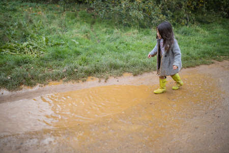Happy little girl looking at muddy puddle before jumping in it