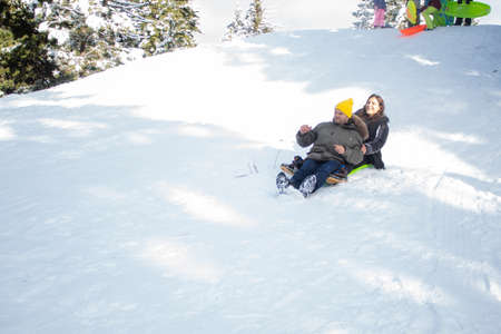 Happy young couple going down a small snowy hill on a sledの写真素材