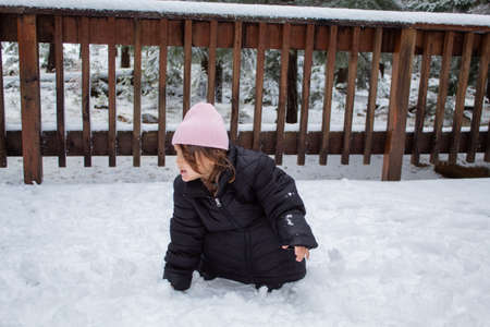 Happy little girl wearing an oversized jacket and playing on the snow