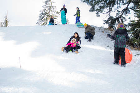 Happy young family going down a small snowy hill on a sledのeditorial素材