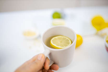 Female hand holding a cup of lemon tea above limes and lemonsの写真素材