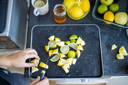 Female hands slicing lemons and limes on a black trayの写真素材
