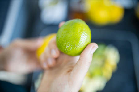 Female hand holding a lime above slices of limes and lemonsの写真素材