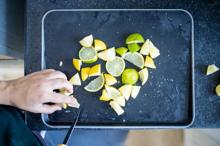 Female hands slicing lemons and limes on a black trayの写真素材