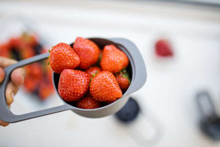 Measuring cup full of fresh strawberries above berries in plastic containers