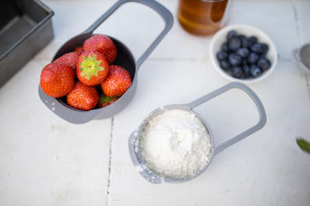 Strawberries and flour in measuring cups above white counterの写真素材