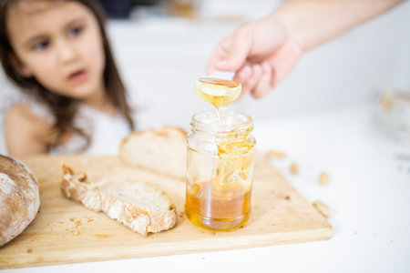 Male hand picking honey from a jar next to a slice of breadの写真素材