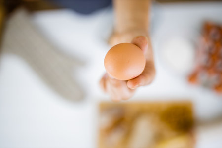 Female hand holding an egg above ingredients on a tableの写真素材