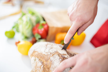 Male hands slicing bread on a cutting boardの写真素材
