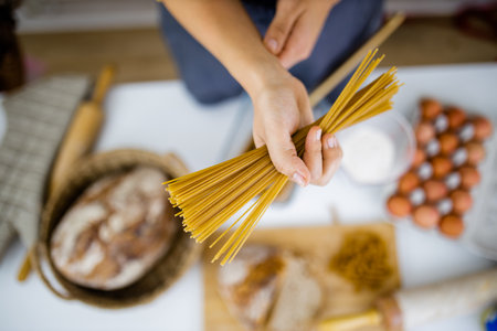 Female hand holding uncooked spaghetti above ingredients on a tableの写真素材