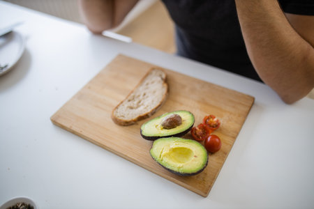 Sliced bread, an avocado cut in half, and tomatoes on cutting boardの写真素材