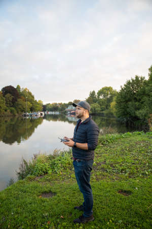 Man standing next to a lake holding a remote control