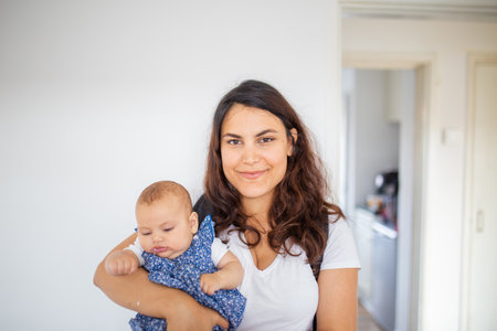Happy woman holding her adorable baby inside a white bedroomの写真素材