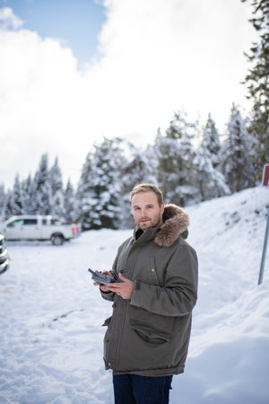 Handsome man holding a remote control with a snowy forest as background