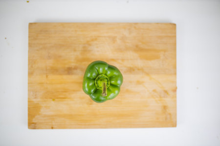 Green bell pepper on a cutting board above a white tableの写真素材