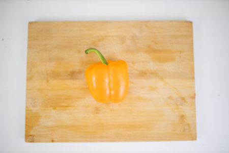 Orange bell pepper on a cutting board above a white tableの写真素材
