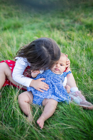 Adorable little girl sitting on the grass and hugging a babyの写真素材