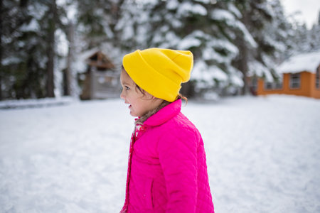 Happy little girl wearing a pink coat in snowy forestの写真素材
