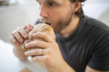 Surprised-looking man at a white table eating breadの写真素材