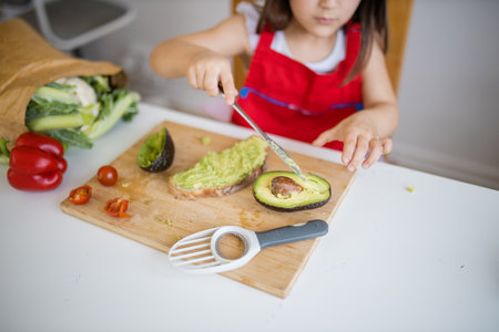 Little girl at a table spreading avocado on a slice of bread