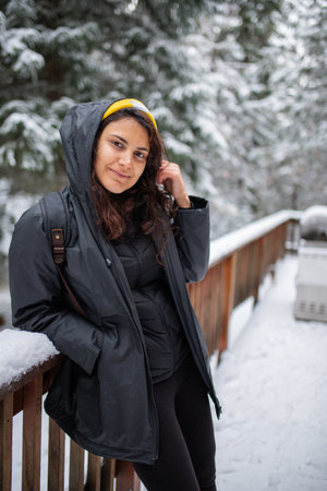 Woman leaning against snow-covered handrail with snowy pines as background