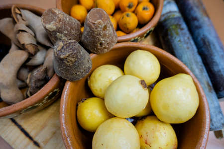 Dark brown sugar canes between clay bowls of fruit