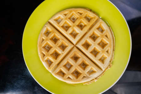 Fresh round waffle on a yellow plate from above