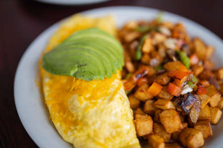 Omelette, roasted potatoes and avocado slices on a white plate