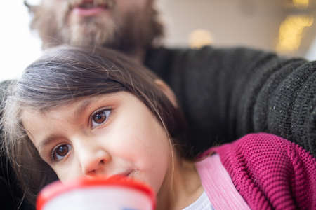 Cute little girl hugged by her father and drinking from a cup