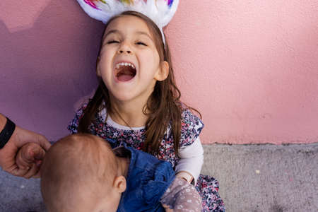 Adorable little girl wearing unicorn headband hugging and kissing a babyの写真素材