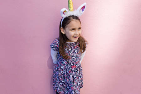 Adorable little girl wearing a unicorn headband with pink backgroundの写真素材