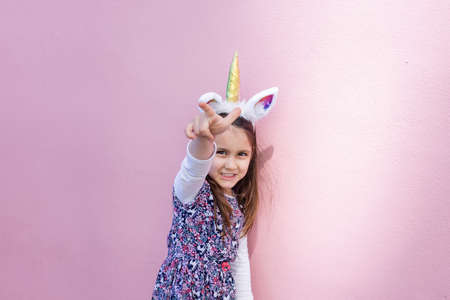 Adorable little girl wearing a unicorn headband with pink backgroundの写真素材