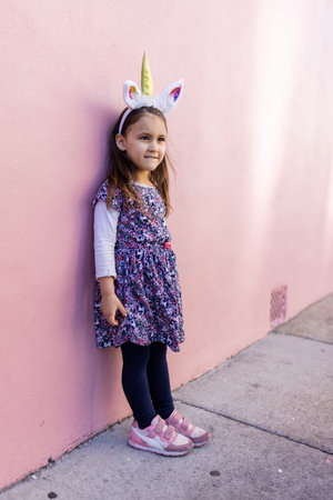 Adorable little girl wearing a unicorn headband with pink background