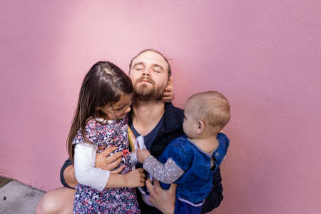 Happy father hugging his two adorable daughters in front of a pink wallの写真素材