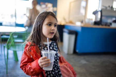 Adorable happy little girl holding a plastic cup in restaurant